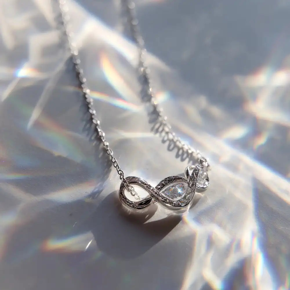 Silberne Unendlichkeitskette mit einem zentralen Edelstein, der auf einer reflektierenden Oberfläche dargestellt ist.