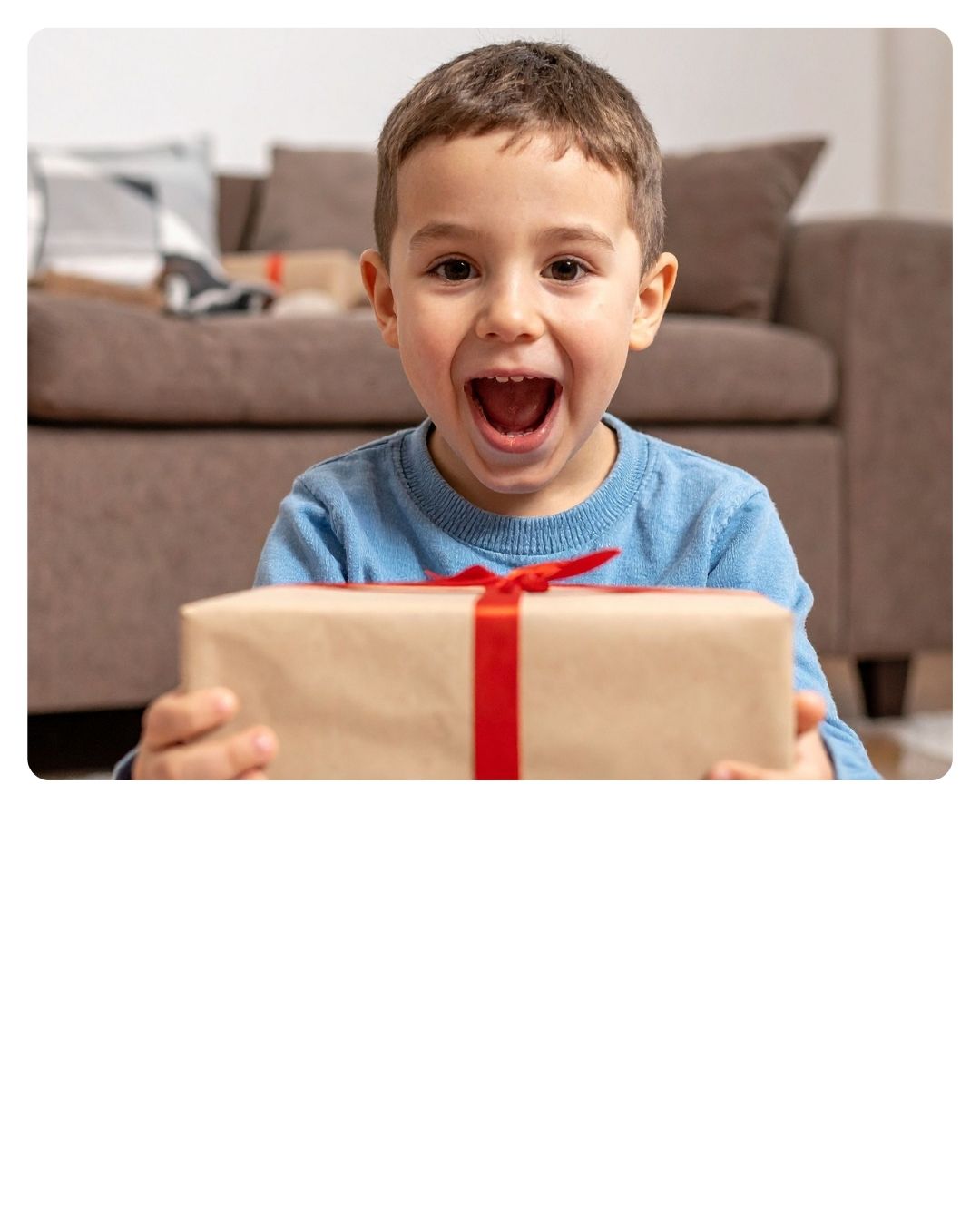 Aufgeregter Junge, der ein eingepacktes Geschenk mit roter Schleife hält.