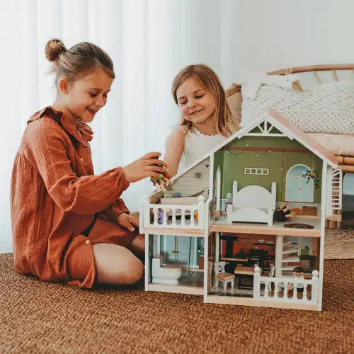Zwei junge Mädchen spielen fröhlich mit einem Puppenhaus auf einem Teppichboden.
