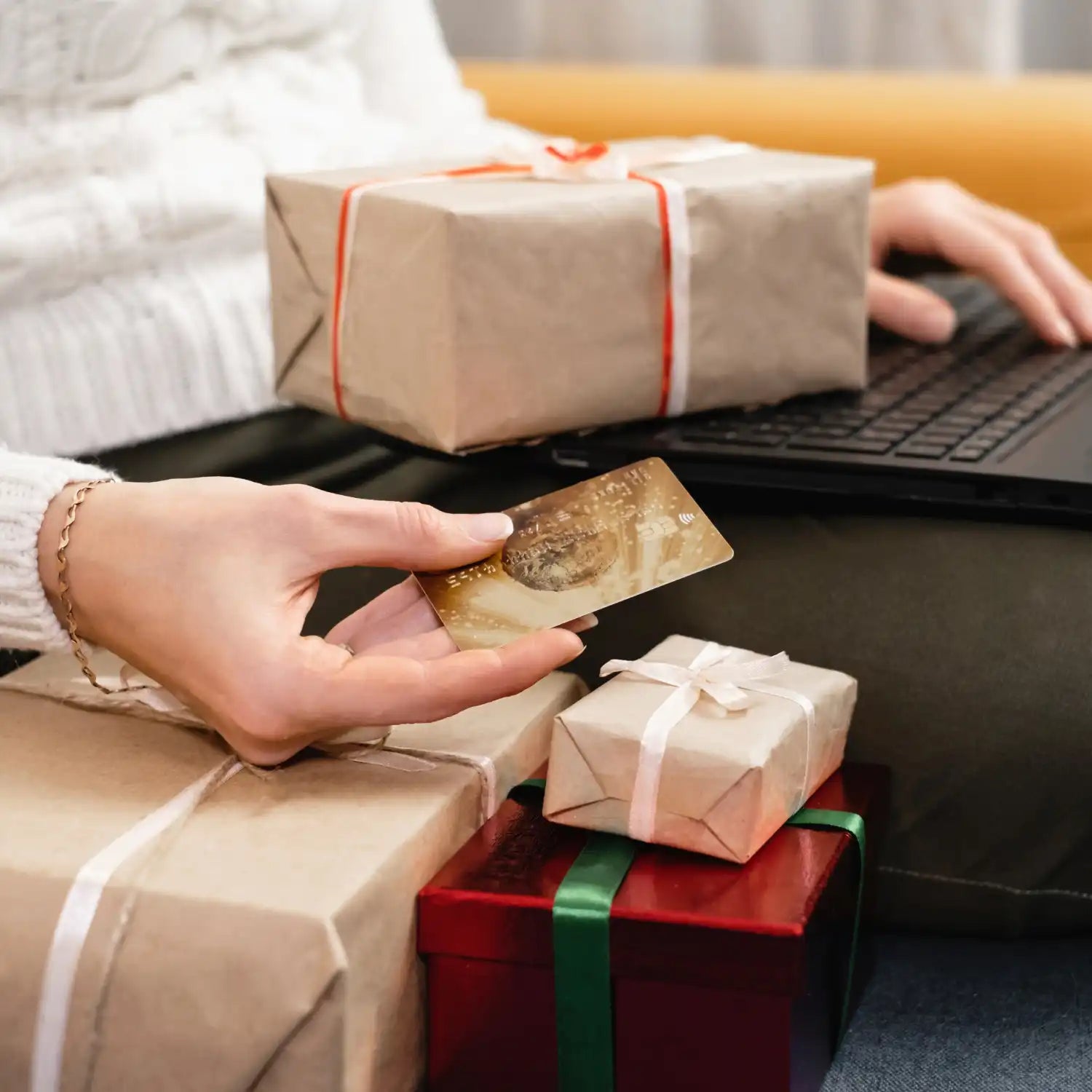 Person, die online mit Kreditkarte einkauft, umgeben von verpackten Geschenkkartons.