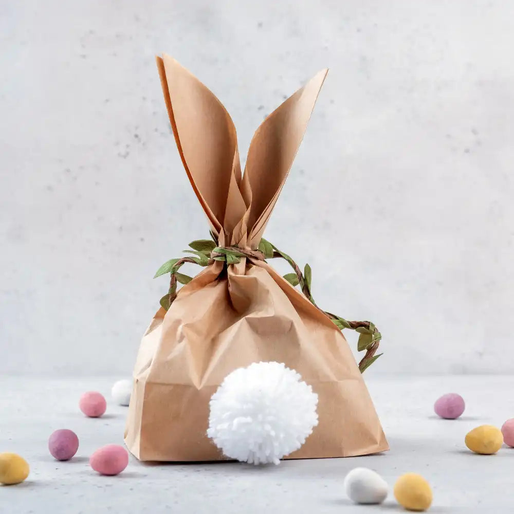 Eine Geschenktüte, die wie ein Hase eingewickelt ist und in der Süßigkeiten-Eier verstreut sind.