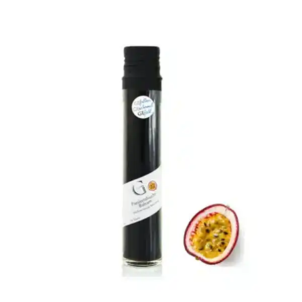 Große Flasche mit dunkler Flüssigkeit neben einer halbierten Passionsfrucht auf weißem Hintergrund.