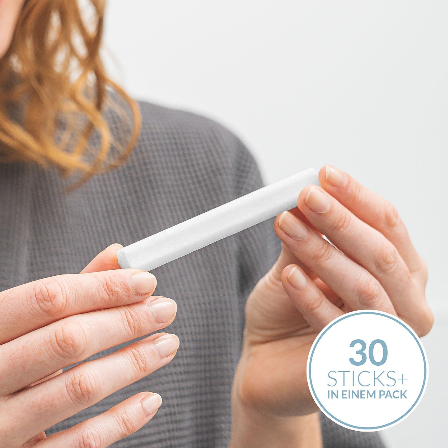 Jemand hält sanft einen weißen Zylinder vor einen grauen Hintergrund mit der Aufschrift „30 Stäbchen+ in einer Packung“. Deine Salzdusche für Zuhause bietet diese beruhigenden, mit Meersalz angereicherten Sticks, ideal für empfindliche Haut.