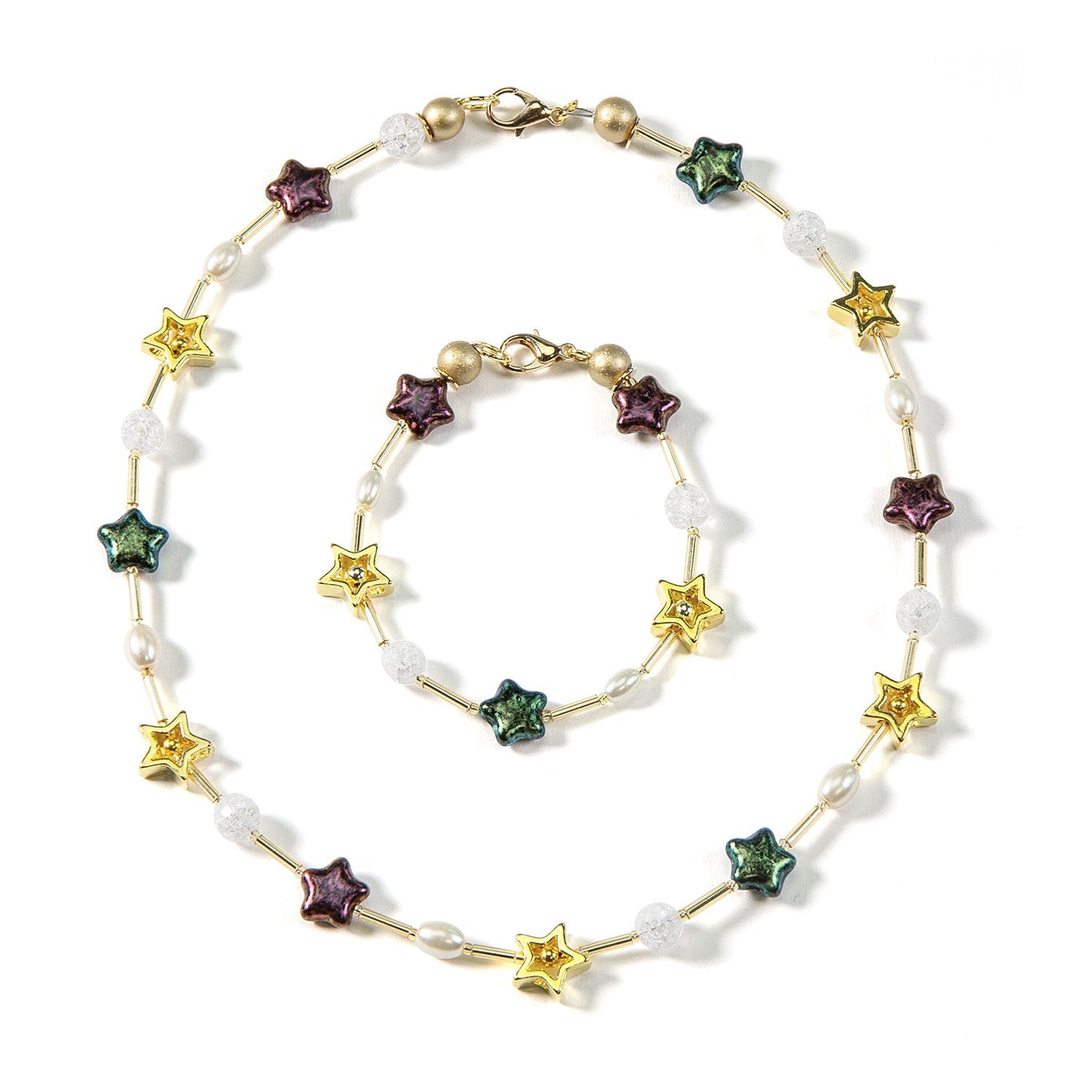 Das Schmuckset „Sterntaler“ besticht durch festliche Eleganz mit farbenfrohen sternförmigen Perlen, weißen Perlen und klar strukturierten Kugeln. Auf weißem Grund glänzt das Set aus Halskette und Armband mit goldenen Verschlüssen und zylindrischen vergoldeten Sternengliedern.