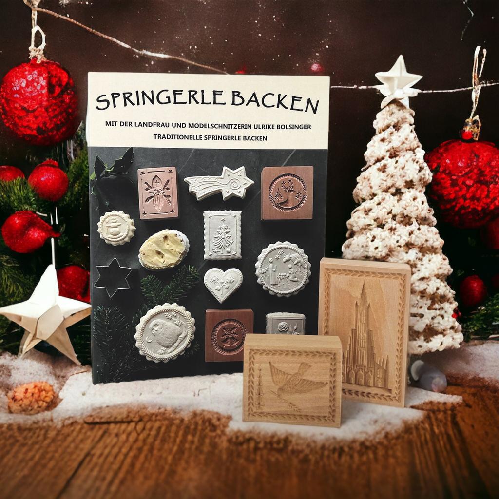 Ein „Set mit 2 Holzspringerle und Buchspringerle-Backen“ wird vor einer festlichen Kulisse mit Ornamenten, einem Baum und Sternen präsentiert. Die Schachtel mit Herz- und geometrischen Motiven eignet sich ideal für die Herstellung traditioneller Weihnachtsgebäcke mit handgeschnitzten Formen.