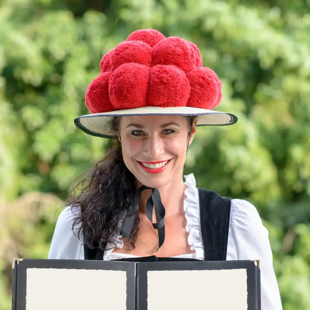 Frau in traditioneller Kleidung mit roter Bommelmütze, lächelnd im Freien.