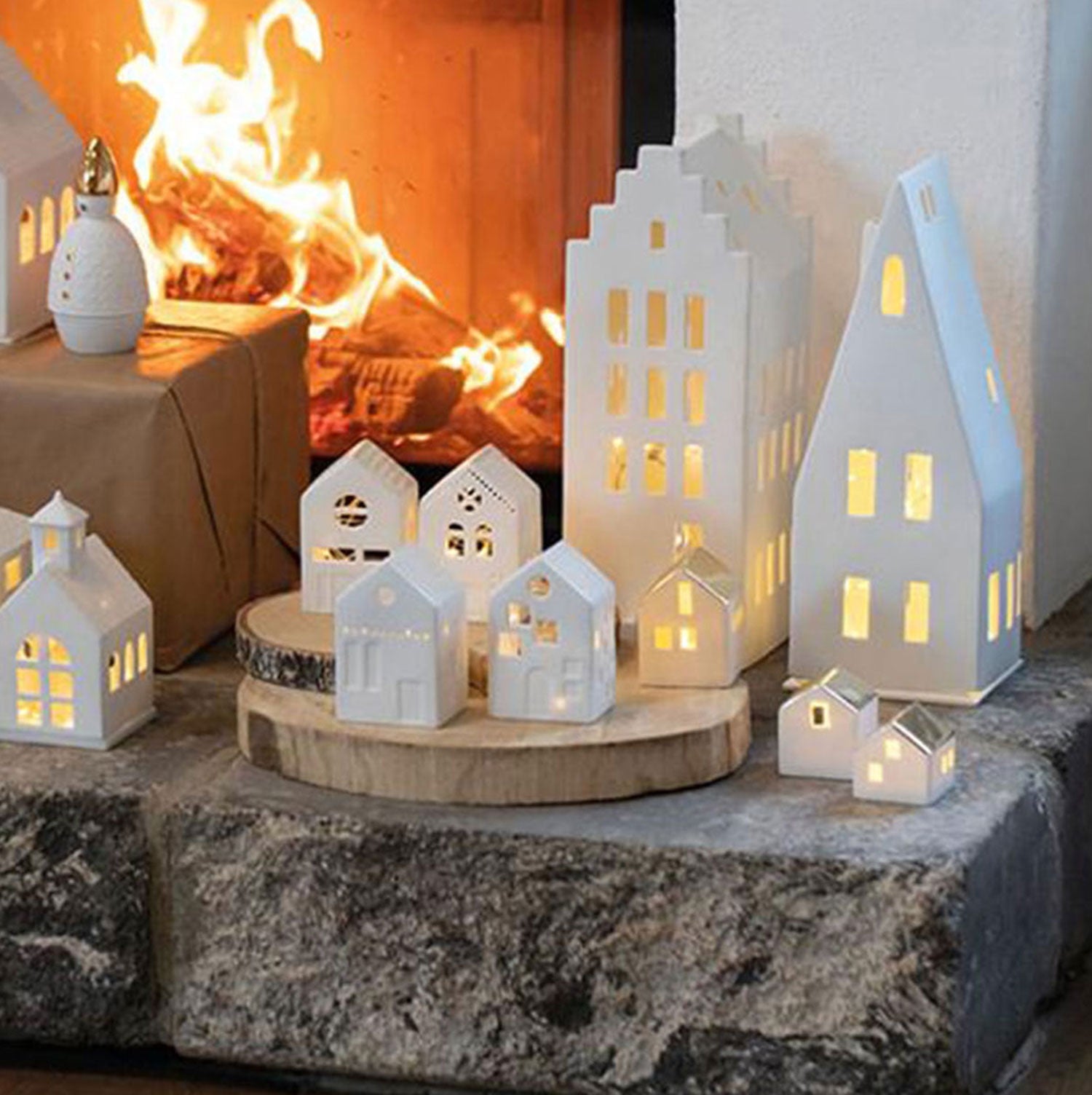 Das Große Lichthaus „Giebeldach“ präsentiert sich auf einem Steinkamin vor einem brennenden Kamin, dessen Fenster vom Kerzenlicht erhellt werden und eine warme, gemütliche Atmosphäre im Raum schaffen.