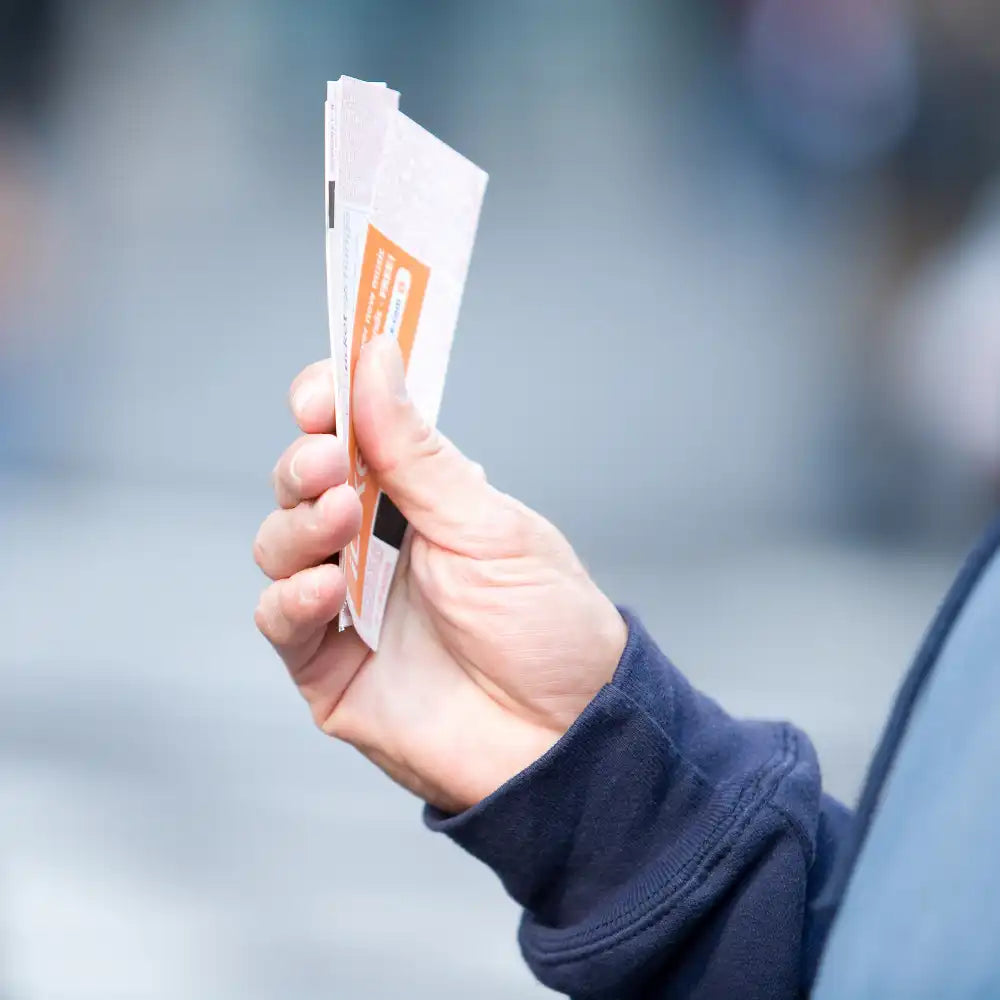 Eine Hand hält mehrere Veranstaltungs- oder Eintrittskarten im Freien.