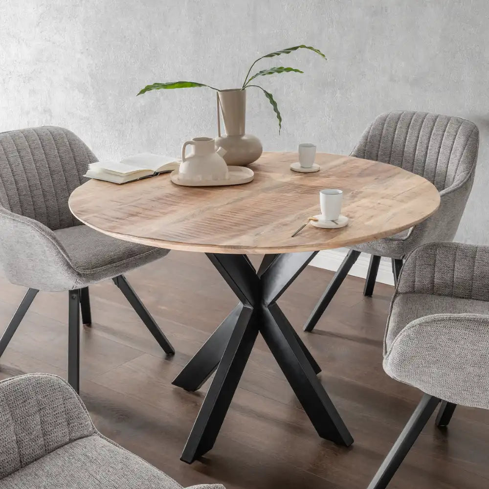 Runder Holztisch mit grauen Stühlen, einer Vase mit Blättern, Tassen und Büchern.