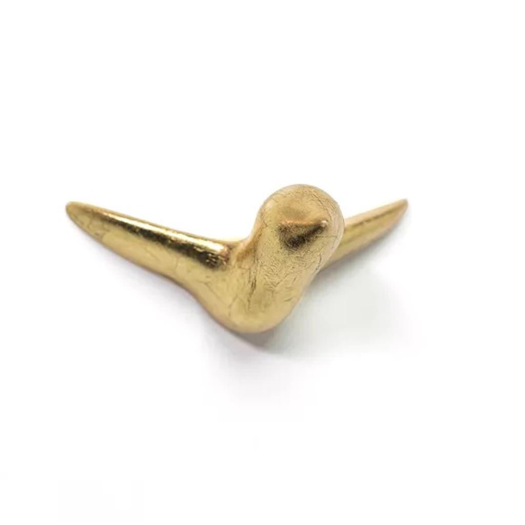 Die Wandskulptur Mini Vogel ist eine kleine, glatte, goldfarbene Vogelskulptur aus Keramik mit ausgebreiteten Flügeln, ideal als minimalistische Wanddekoration vor einem schlichten weißen Hintergrund.