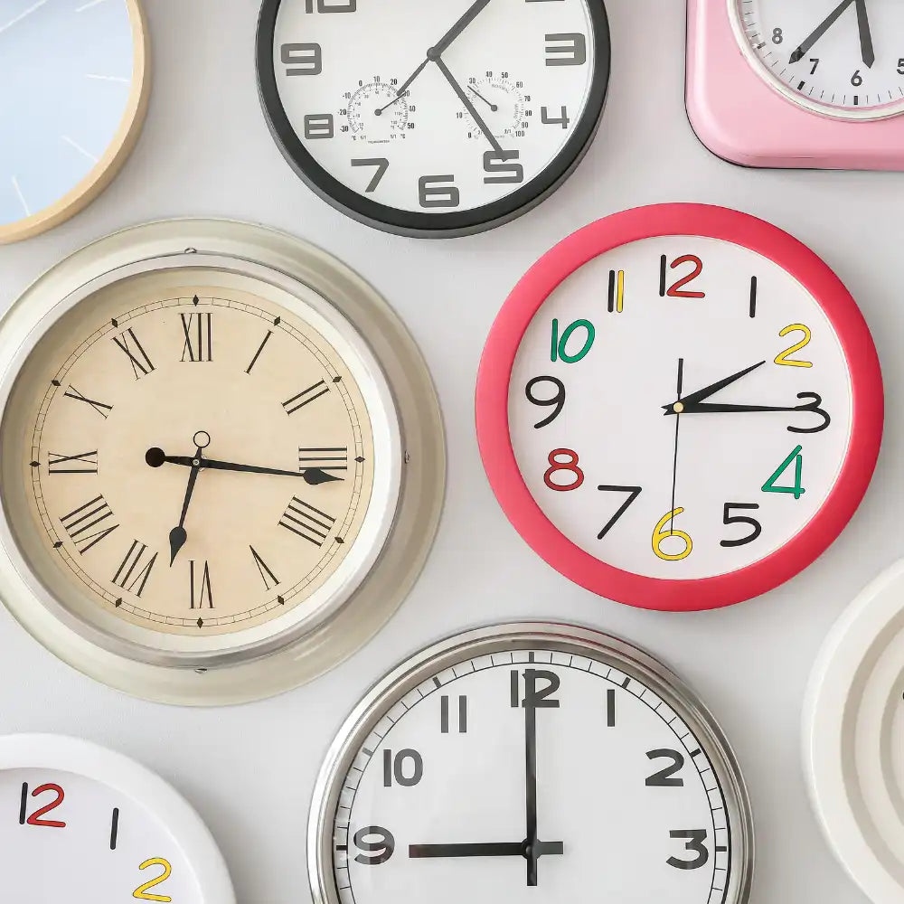 Verschiedene Wanduhren mit unterschiedlichen Stilen und Farben auf einer weißen Wand.